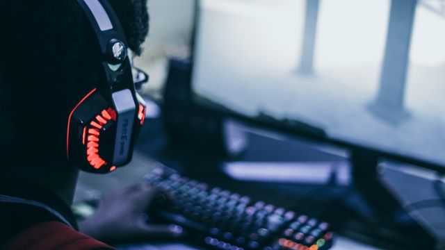 A person with gaming headset playing games on a gaming pc and there is a mechanical keyboard in front of him.